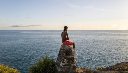 A young boy is sitting on a rock looking out at a calm ocean.