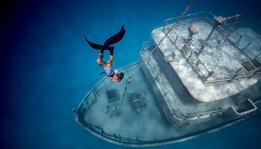 A man free diving in clear waters near sunken shipwreck.