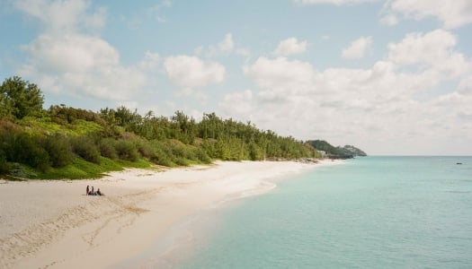 A wide shot of a small group of people sitting on a vacant pristine beach. 