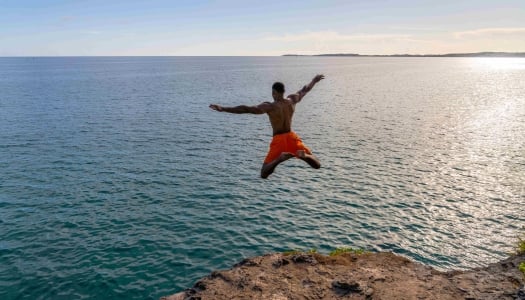 A man is star jumping into the ocean from a cliff.
