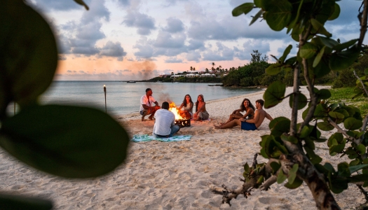 A group of friends are sitting on the beach around a bonfrie.