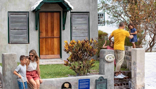A family is sitting by a grey house with a wooden door.