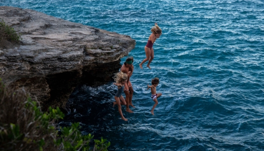 A family is jumping off a small cliff into the water. 