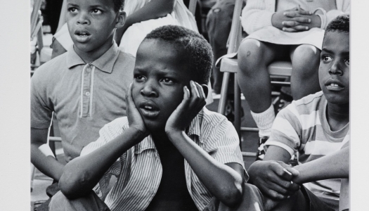 A group of young black children are watching a street theatre.