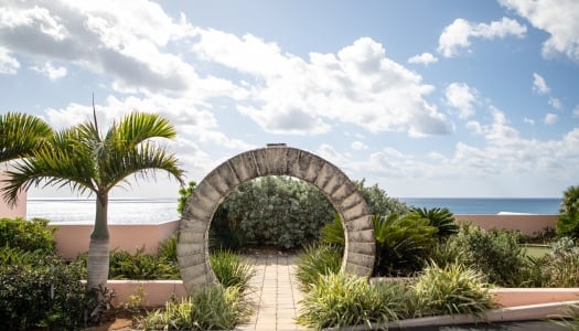 A wide angle of a Bermuda moon gate with calm waters and pink building in the background.