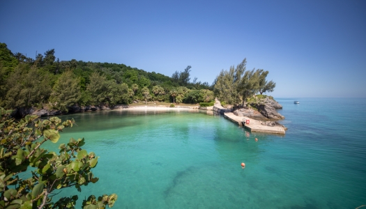 a view of a nearly empty pristine beach with calm waters and a boat in the distance.