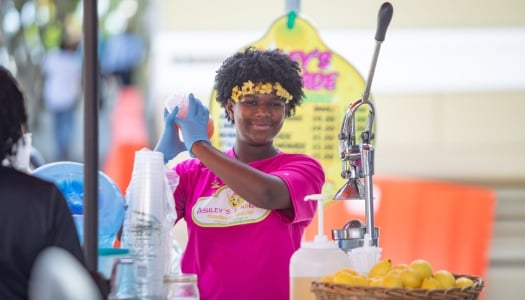 A girl is smiling at the camera making lemonade.
