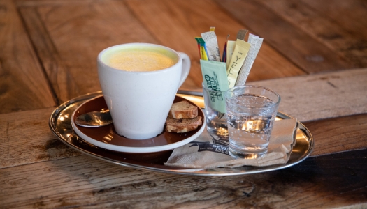 A close up of a tray with a coffee cup, sugar, and sparkling water. 