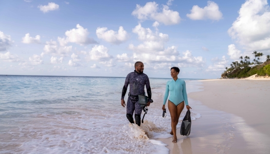 Two people are walking along the beach with scuba gear. 
