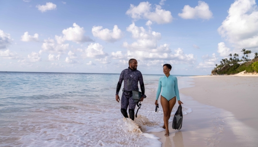 Two people are walking along the beach with scuba gear.