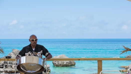 A man is playing a steel drum by the beach.