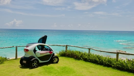 A twizy is on the grass by the calm blue ocean.