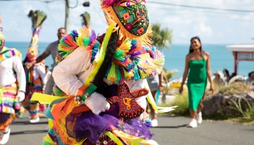 A close up of a gombey dancer with people dancing and walking behind.