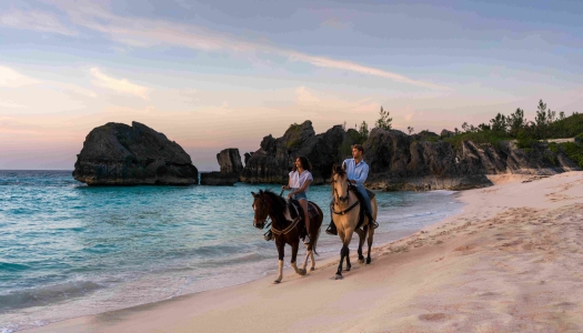 Two people are riding horses at sunset on the beach.