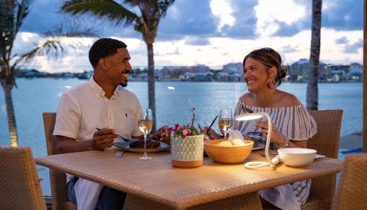 A couple is sitting at a dining table with a scenic background.