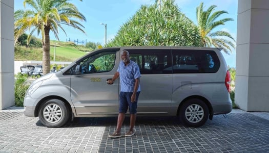 A taxi driver is standing holding the door to the passenger seat.