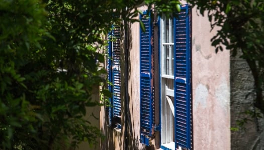 An exterior of an old building with blue shutters and fading pink walls.