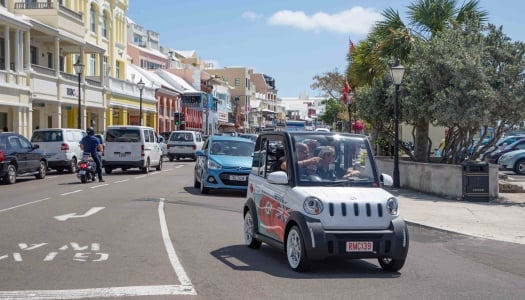 A couple is driving on front street in a microcar.