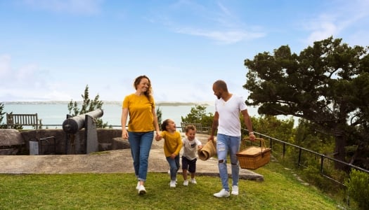 A family is on a hill having a picnic with a scenic ocean view in the background.