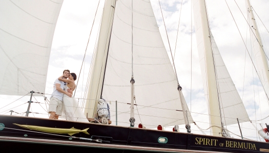A couple is hugging on an old sail boat.