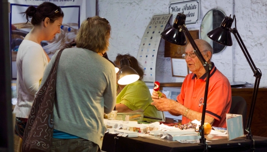 A man is showing his crafts to two women at the Bermuda Craft Market.