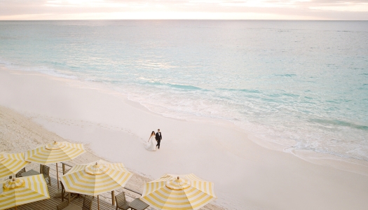 A couple is walking along the beach in their wedding attire.