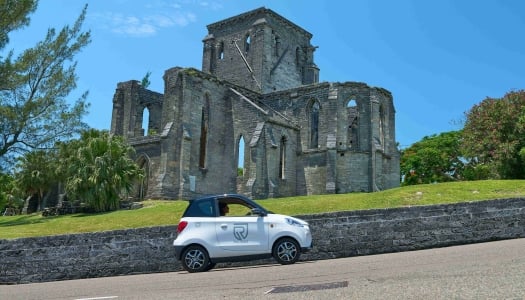 A person is driving an electric microcar by a scenic building.