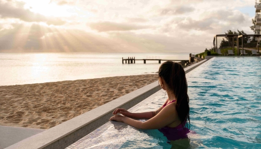A woman is standing in a pool looking at sunrise.