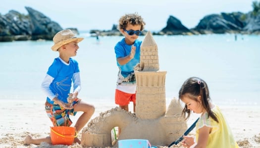 A group of kids are playing in the sand at the Hamilton Princess Beach Club