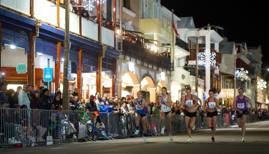 A group of women are running on Front Street with a crowd looking on.