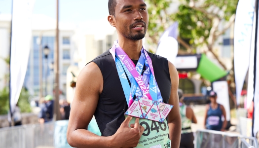 A man is standing holding four medals during the Chubb Triangle Challenge.