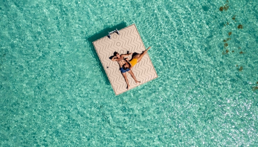 A couple is cuddling while floating on a dock surrounded by turquoise waters.