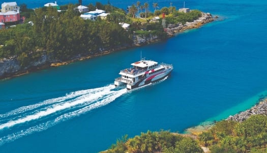 A ferry is riding out of St. George's with calm blue waters.