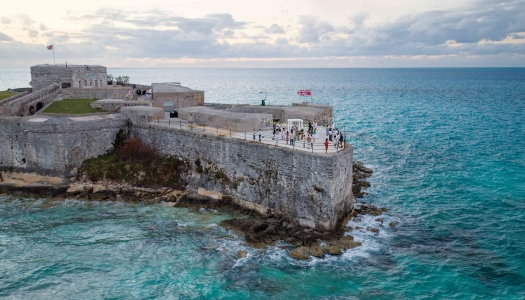 A group of people are standing in an old scenic fort by the water.