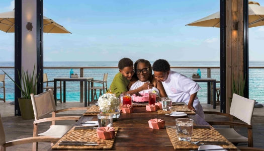 A woman and two children are celebrating a birthday a table with an ocean view in the background.