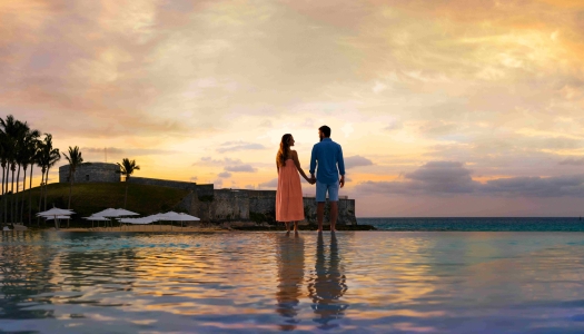 A couple is standing by a pool with sunset in the background.