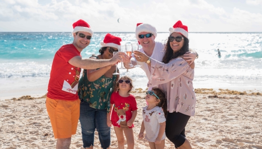 A family is cheering while on the beach in Christmas gear.