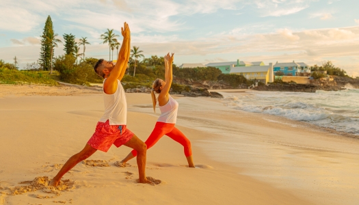 A couple is doing yoga on the beach at sunset.