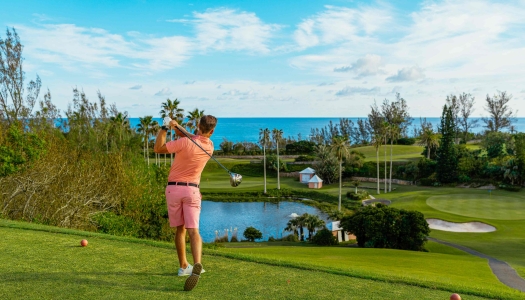 A man is teeing off on a scenic course with the ocean in the background.