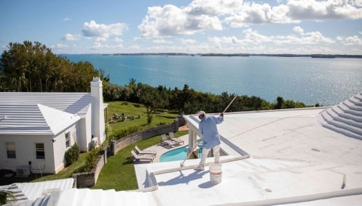 A man is painting a Bermuda roof with white paint.