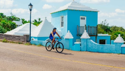 A man is riding a bike next to a blue pastel building.