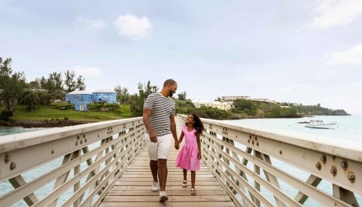 A father and daughter are walking along a bridge smiling.