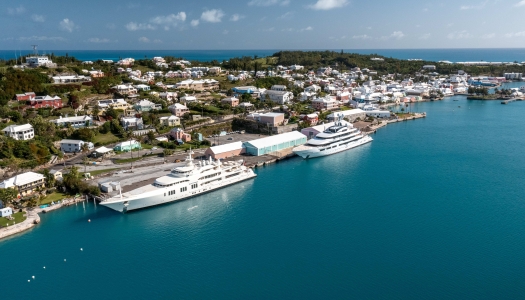 Aerial view of dock with two superyachts and calm blue waters.