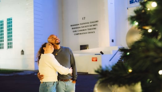 A couple are posing by a Christmas tree.
