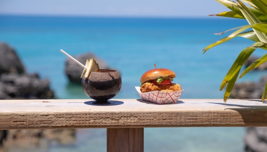 A beach cocktail and a fish sandwich with a waterview in the background