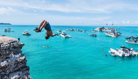 A person doing a backflip off a rock into the sparkling blue waters of Bermuda