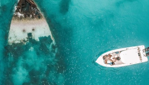 A boat approaches a Bermuda shipwreck visible through the clear, turquoise waters.