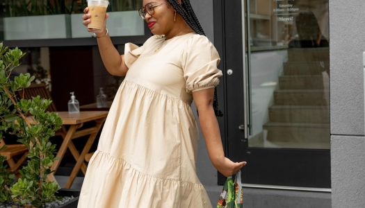 A woman in front of a cafe holding up an iced coffee and smiling