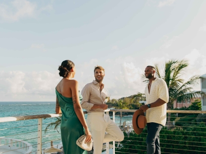 A woman and two men are standing on a balcony laughing. 