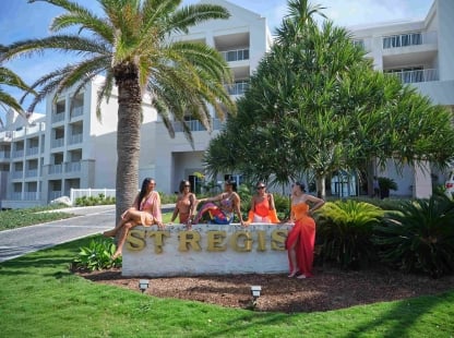 A group of friends are sitting on the St. Regis Bermuda hotel sign.